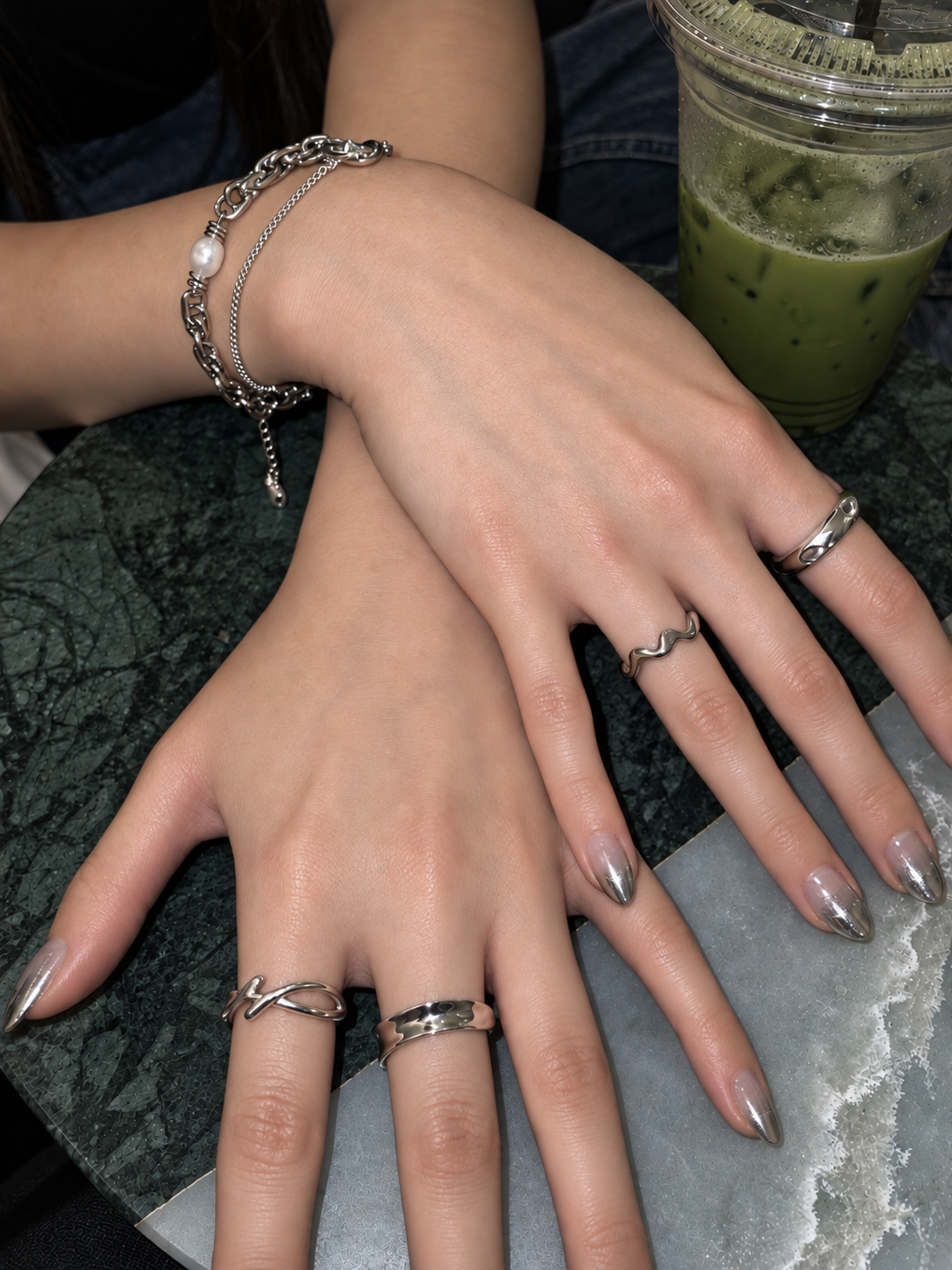 Silver rings and a pearl chain bracelet styled beside an iced matcha